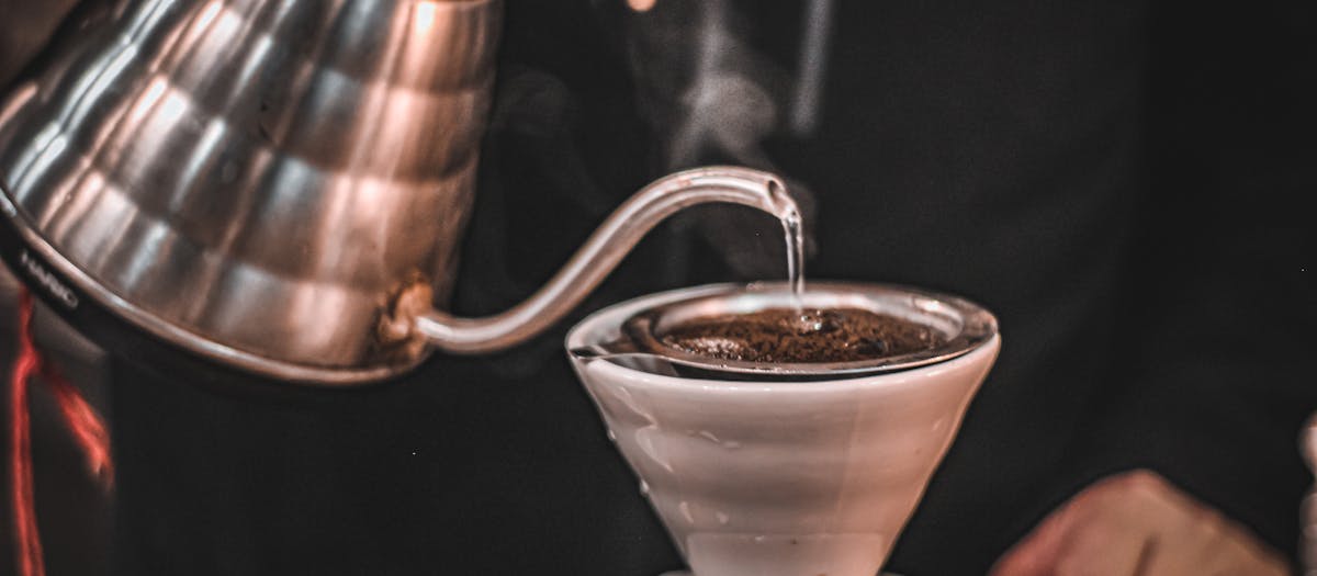 Steam rises as hot water is poured over coffee grounds in a pour-over coffee maker.